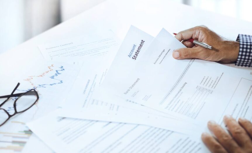 A personal banker sitting at the table with a pile of bank statements in front of them. Their black glasses are next to them.