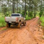 A pickup truck on a reddish muddy road in the middle of a sparsely wooded area on a gray, overcast day.