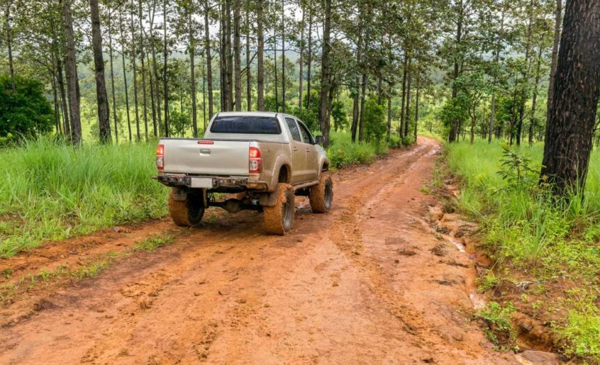 A pickup truck on a reddish muddy road in the middle of a sparsely wooded area on a gray, overcast day.