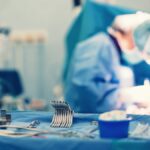 An operating room instrument tray with the tools organized neatly. Surgeons are performing a procedure behind the tray.