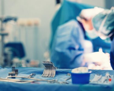 An operating room instrument tray with the tools organized neatly. Surgeons are performing a procedure behind the tray.