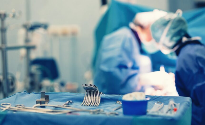 An operating room instrument tray with the tools organized neatly. Surgeons are performing a procedure behind the tray.