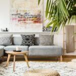 A modern living room with a gray couch, neutral poufs, wooden accessories, and an indoor palm plant.