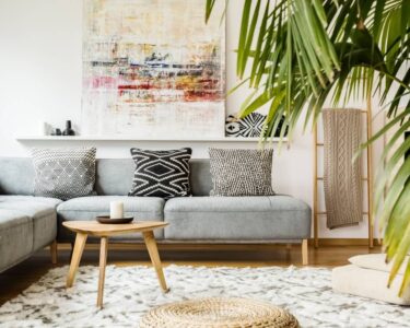 A modern living room with a gray couch, neutral poufs, wooden accessories, and an indoor palm plant.