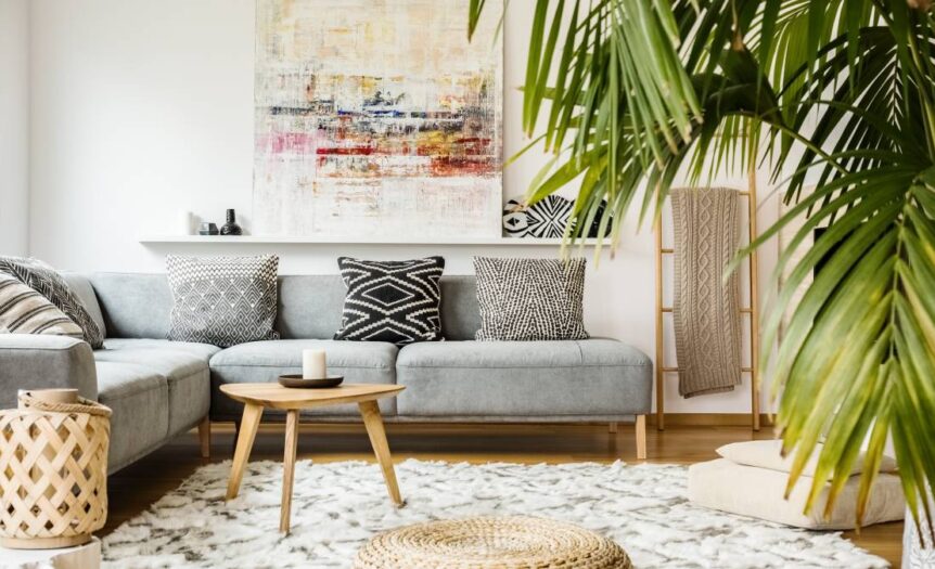 A modern living room with a gray couch, neutral poufs, wooden accessories, and an indoor palm plant.