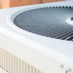 A close-up of the top half of a clean, outdoor HVAC unit. An orange brick wall is in the background of the AC condenser.