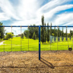 A blue swing set in an empty park built on a patch of mulch. The swing set is surrounded by lush, green grass.