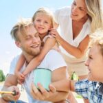 A family of four sits in a boat and takes a fishing trip on a lake. All of the family members have blond hair.