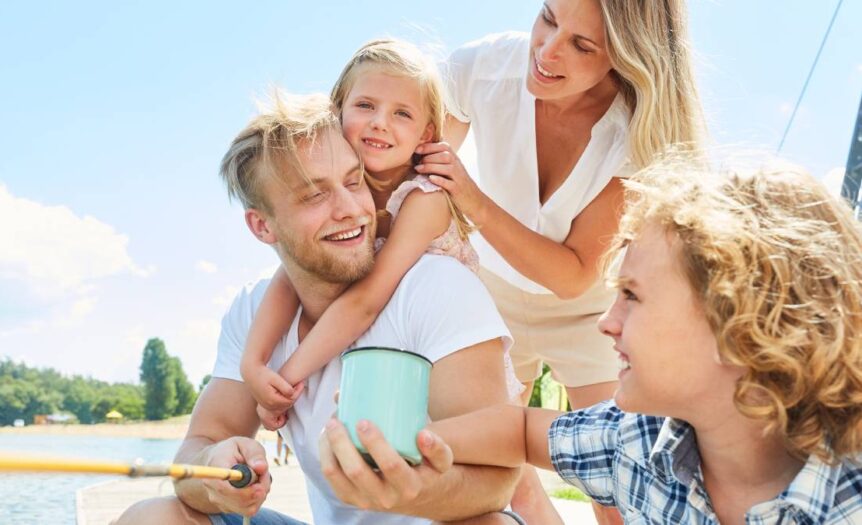 A family of four sits in a boat and takes a fishing trip on a lake. All of the family members have blond hair.