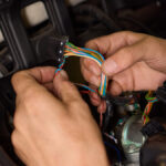 A close-up view shows a person's hands working on a colorful collection of wires inside a vehicle.