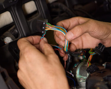 A close-up view shows a person's hands working on a colorful collection of wires inside a vehicle.