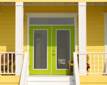 The entry side of a home where stairs lead up to its lime green doors. The walls on the porch are a muted yellow.