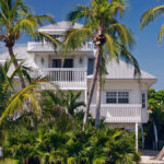 A back-view of a tropical home on the beach in Florida. The house has a modern exterior with palm trees as a barrier.