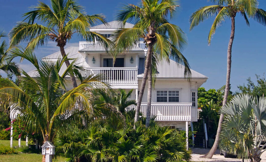 A back-view of a tropical home on the beach in Florida. The house has a modern exterior with palm trees as a barrier.