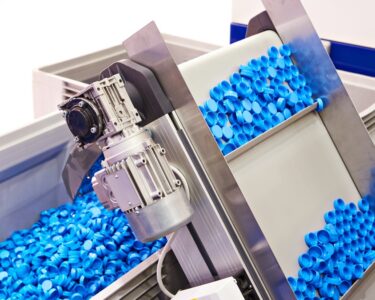 Blue plastic caps sitting on a conveyor machine before they are dropped into a large bin full of other plastic caps.