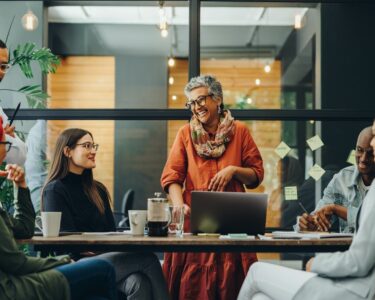 A diverse group of employees smiling and collaborating around a modern boardroom table in a bright, office setting.