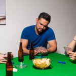 A group of men play a game of poker around a square table with green felt. On the table are playing cards and poker chips.