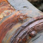 A close up view of a large pipe where the pipe and the seals are completely corroded, turning orange and brown.