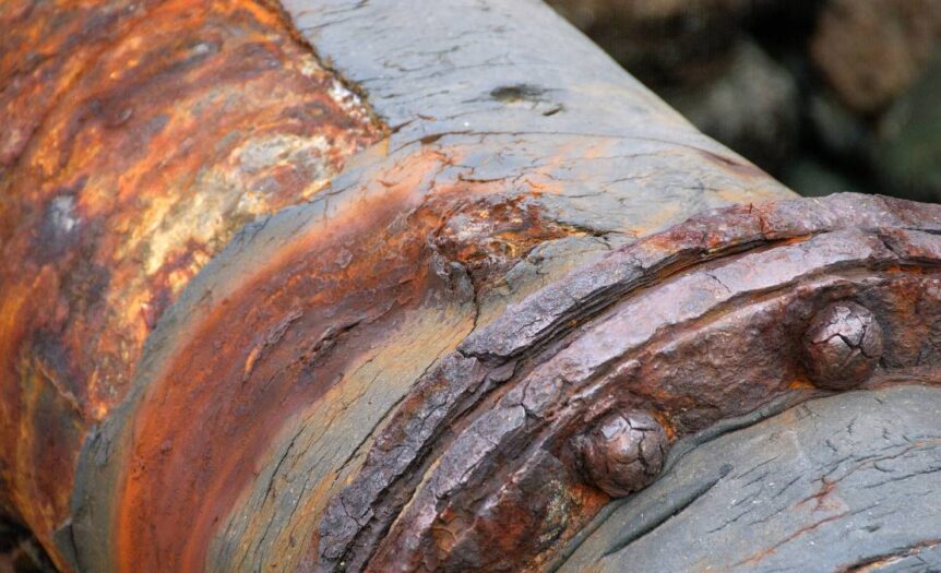 A close up view of a large pipe where the pipe and the seals are completely corroded, turning orange and brown.