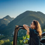 A close-up of a young woman traveling by car in the mountains on a sunny day. She's admiring the mountains.