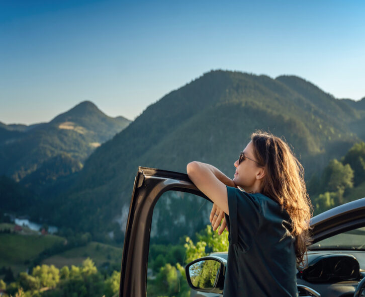 A close-up of a young woman traveling by car in the mountains on a sunny day. She's admiring the mountains.