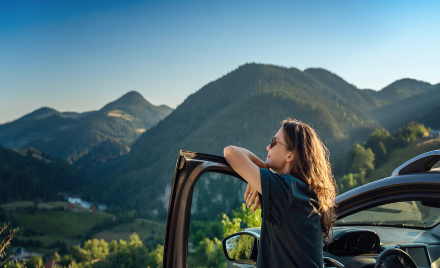 A close-up of a young woman traveling by car in the mountains on a sunny day. She's admiring the mountains.