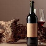 A wine bottle and glass of red wine in front of a piece of weathered wood on a brown background.