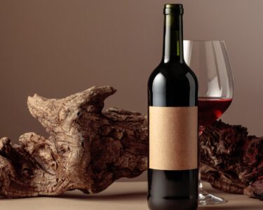 A wine bottle and glass of red wine in front of a piece of weathered wood on a brown background.
