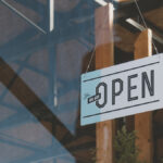 A window to a business with a white sign that says “Yes, we are open” on it in black lettering.