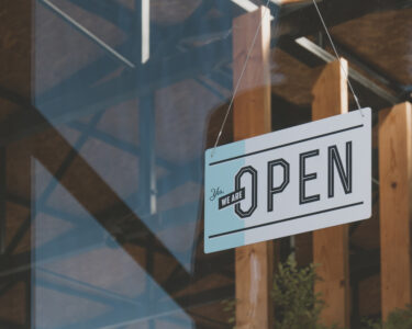 A window to a business with a white sign that says “Yes, we are open” on it in black lettering.