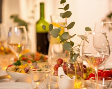 A close-up of a dining room table with wine glasses, a bowl of salad, cherry tomatoes, and a vase with eucalyptus.