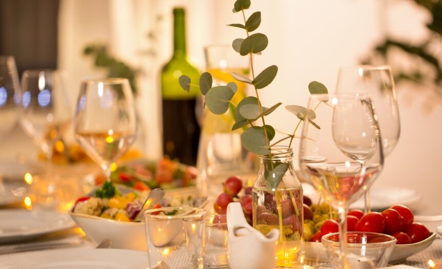 A close-up of a dining room table with wine glasses, a bowl of salad, cherry tomatoes, and a vase with eucalyptus.