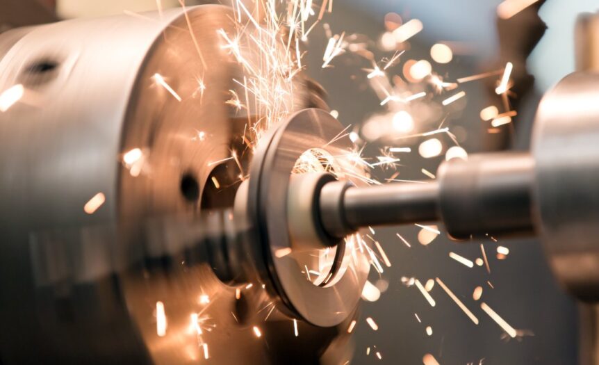 A close-up of a lathe grinder's tailstock spindle, spinning rapidly and producing heat sparks on a jaw chuck.