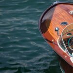 A luxurious, classic boat floats on open water. The bow showcases a polished wooden finish with timeless details.