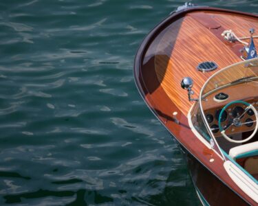 A luxurious, classic boat floats on open water. The bow showcases a polished wooden finish with timeless details.