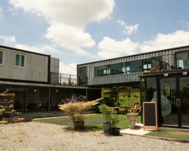 The exterior of a modern two-story building comprised of metal shipping containers with a blue sky in the background.