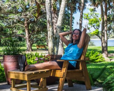 A woman relaxes and lies back in a chair on her patio in Florida. Her patio is beautifully landscaped and green.