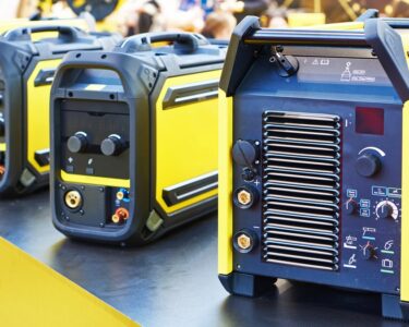 Four yellow and black portable welding machines sit on a counter with a black top and yellow-painted sides.