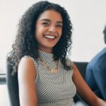 A happy woman with long curly hair is smiling during her meeting with her colleagues in a conference room.