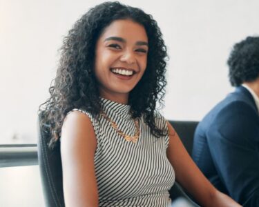 A happy woman with long curly hair is smiling during her meeting with her colleagues in a conference room.