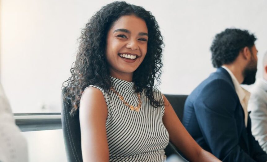 A happy woman with long curly hair is smiling during her meeting with her colleagues in a conference room.