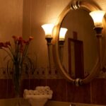 A dimly lit bathroom features a stack of rolled white towels on the sink next to a vase of calla lilies.