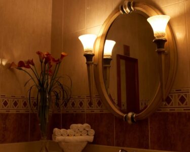 A dimly lit bathroom features a stack of rolled white towels on the sink next to a vase of calla lilies.