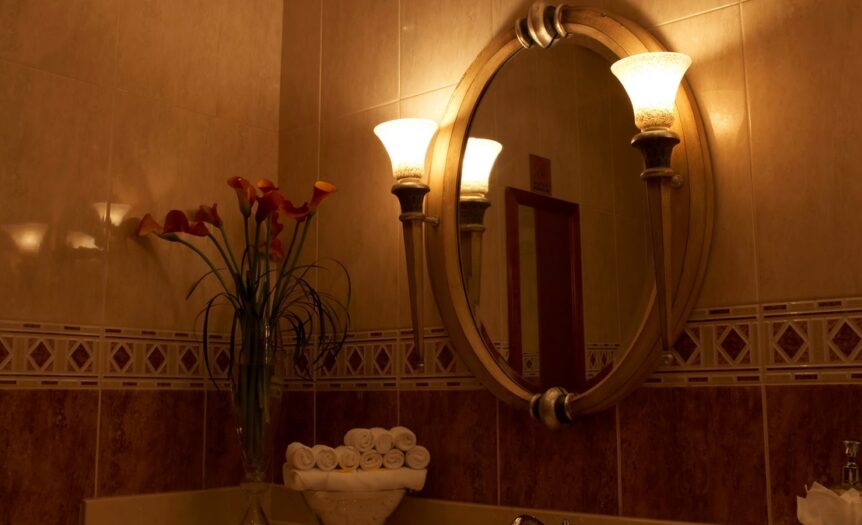 A dimly lit bathroom features a stack of rolled white towels on the sink next to a vase of calla lilies.