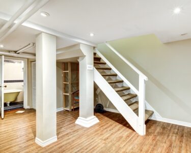 A freshly finished home basement with wood plank flooring, white baseboards, and light beige painted walls.
