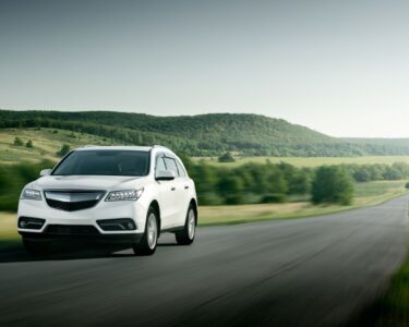 On a large road in the middle of nowhere, surrounded by hills and small trees, a small white car drives down the road.