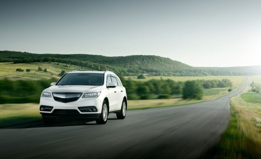 On a large road in the middle of nowhere, surrounded by hills and small trees, a small white car drives down the road.