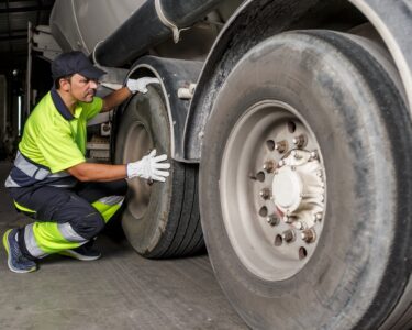 A trailer hauler kneeling on the ground next to their trailer's large tires. They are wearing neon yellow safety gear.