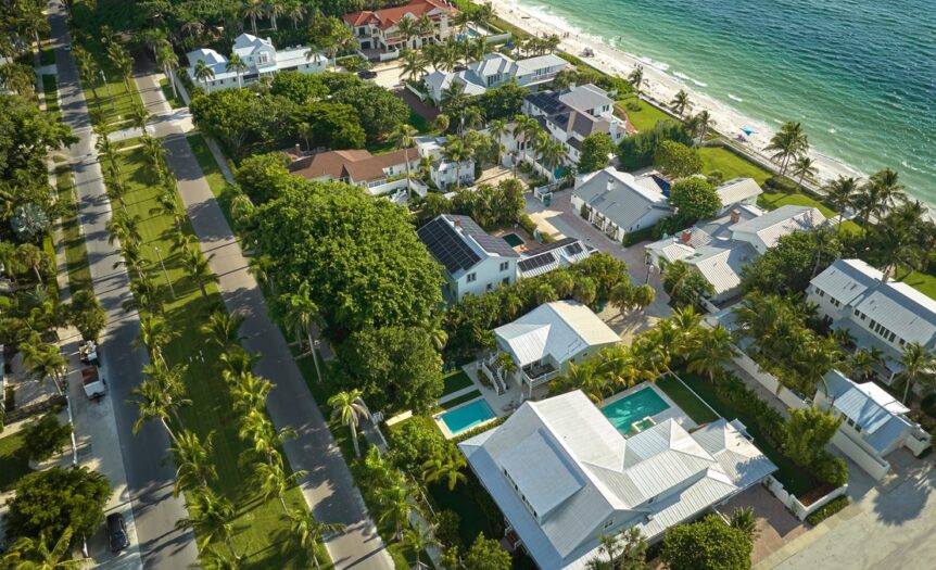 An aerial view of a small neighborhood. A beach is visible on the right and there are two main roads going through the area.