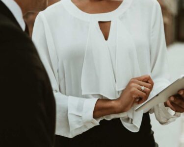 A woman, who has a wedding ring on their left finger, is using digital device to show something to someone.